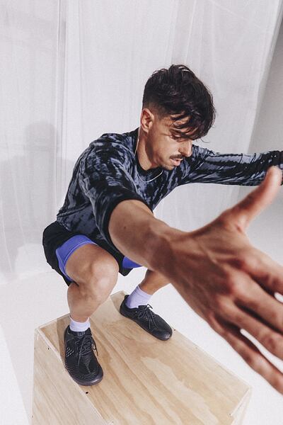 Mladý muž, dělající dřep, ruce má zvednuté a na noze VIVOBAREFOOT boty. 